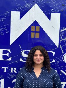 Woman with curly hair smiles in front of a blue and white logo.